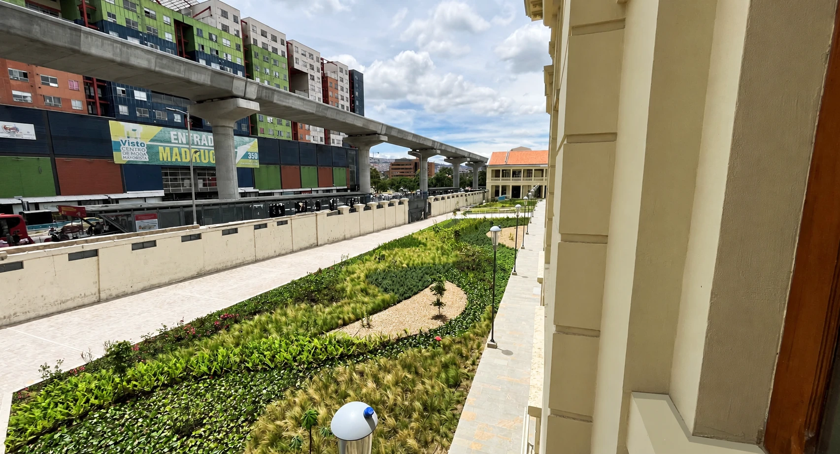 Jardín con gramíneas y plantas verdes entre un andén y un edificio patrimonial, con el viaducto al fondo