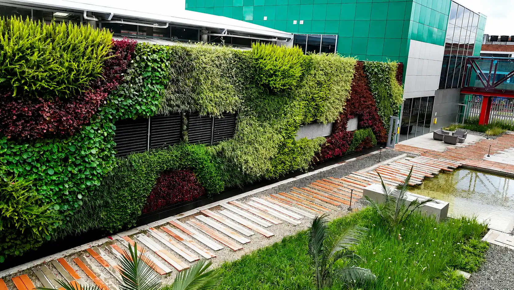 Muro verde de gran formato junto a un sendero de madera y un espejo de agua