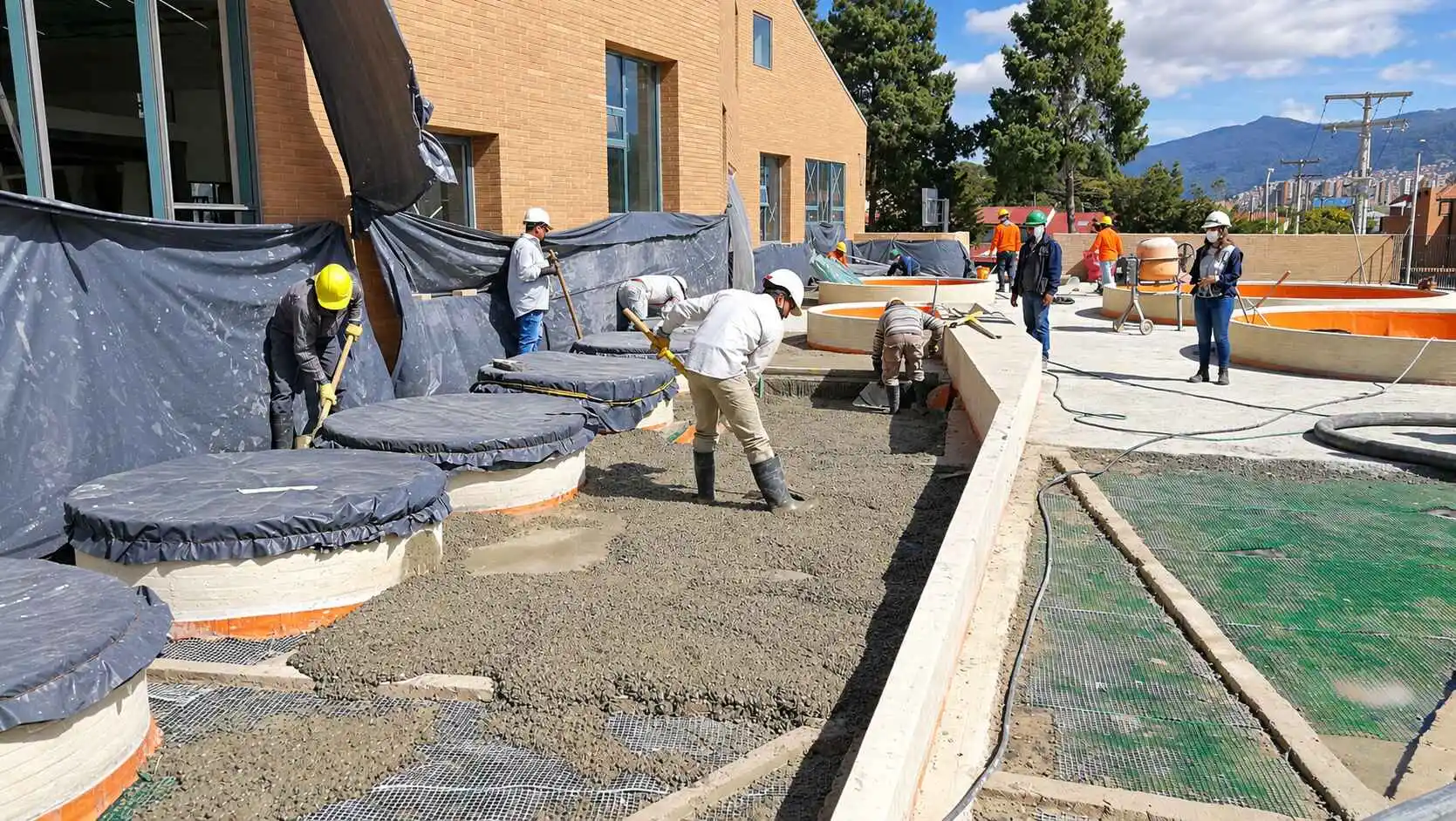 Obreros construyendo una terraza con cubiertas circulares junto a un edificio de ladrillo