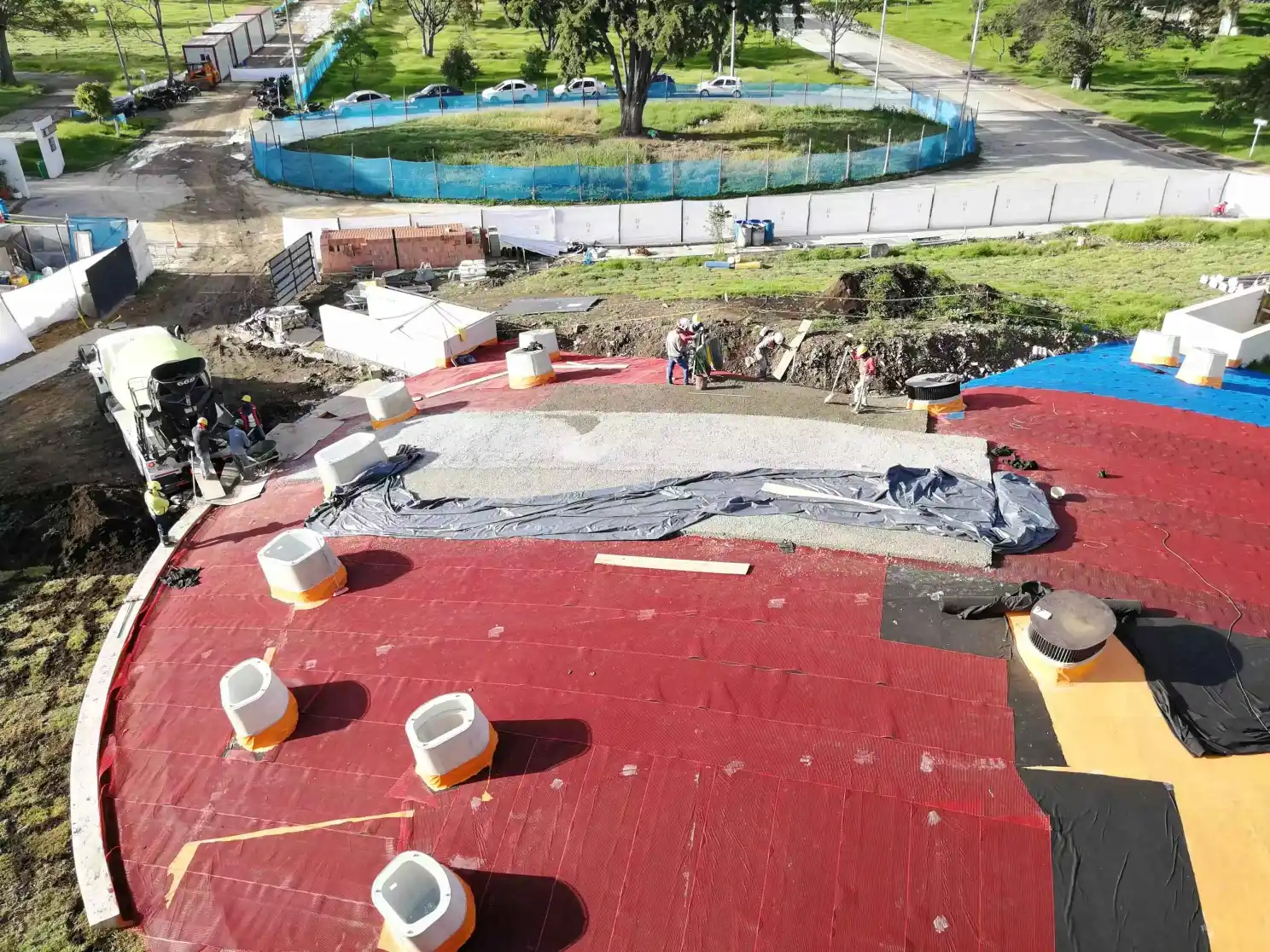 Obra de una cubierta circular en construcción con membrana roja, cuadrilla y mezcladora de concreto